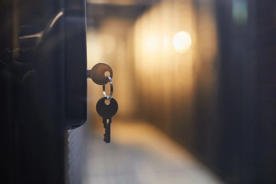 Gros plan sur des clés suspendues à une serrure de porte dans un couloir faiblement éclairé sur fond flou, créant une ambiance lunatique et mystérieuse