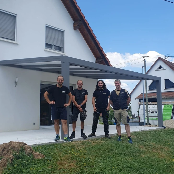 Un artisan en casquette rouge et t-shirt gris travaille sur une structure de pergola en bois